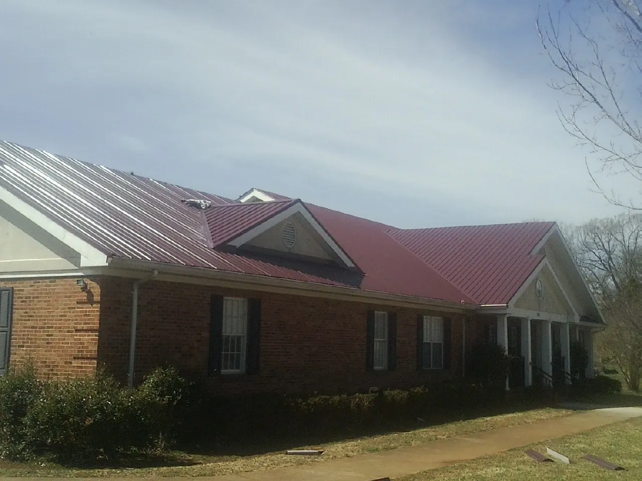 Red metal roof with gabled entries on a long brick building, from a Hail Damage Roof Repair job in Mount Pleasant
