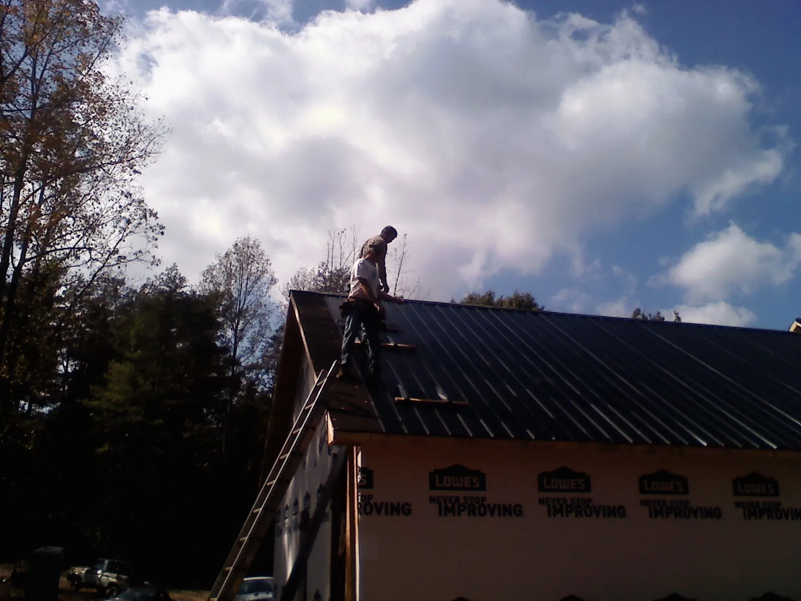 Roofer fastening dark metal panels high against a cloudy sky, from a Roof Inspection job in Mount Pleasant