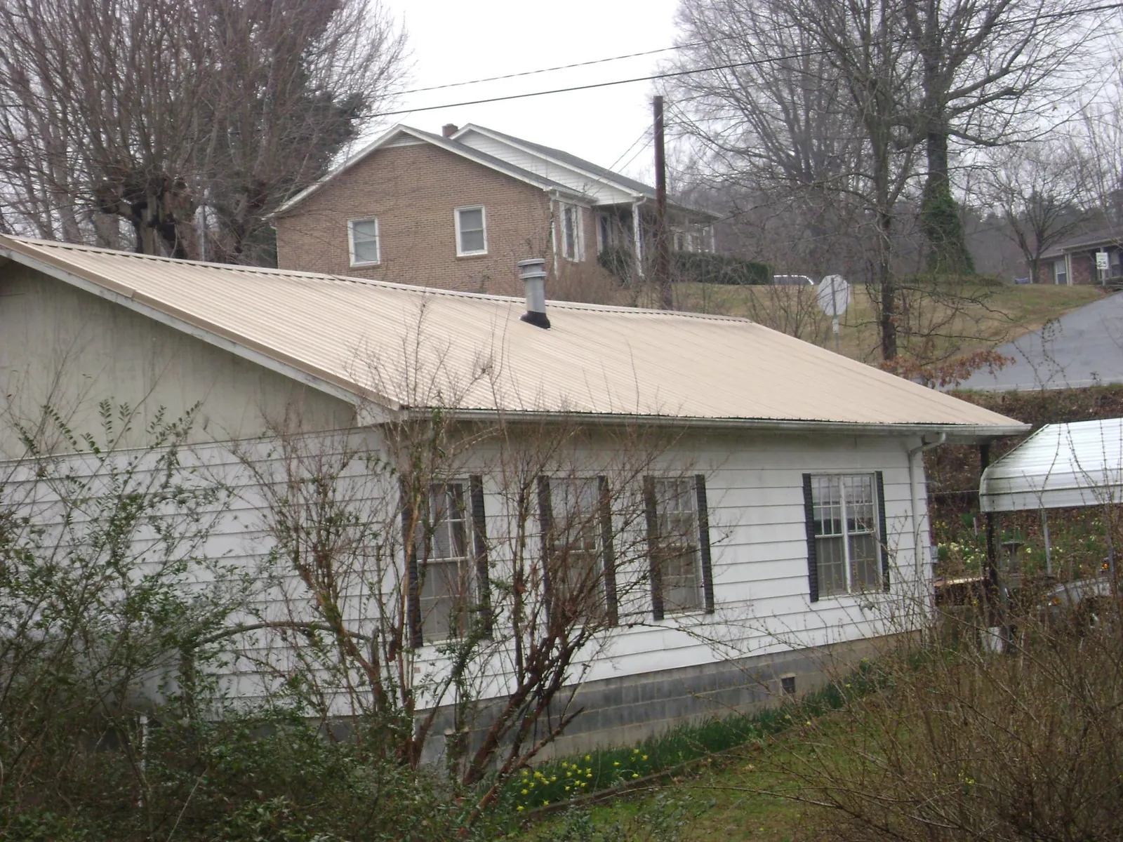 Tan metal roof on a white sided house set into a hillside — Commercial Roofing by Roofing Brothers in Mount Pleasant